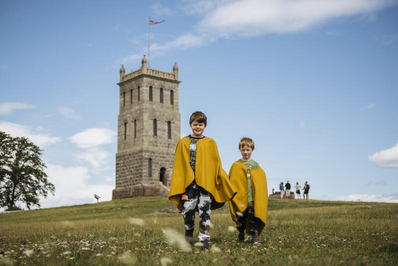 To gutter med gule kapper står foran Slottsfjelltårnet. Det er sol og sommer