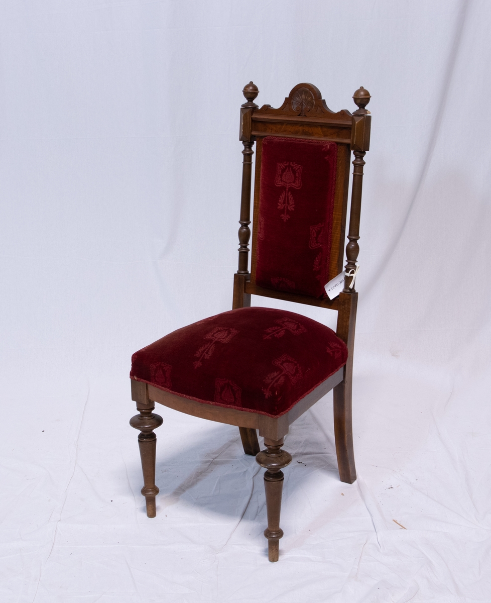 Stoler med høy rygg og dreide ben. Setetog stolryggen er polstret og trukket med rød fløyel. Stoffet har også et dekorativt mønster bestående av endring i tekstur. Treverket på stolryggen er dreid og utskåret i mønster ved toppen. To kuler kroner hver side av stolryggen.