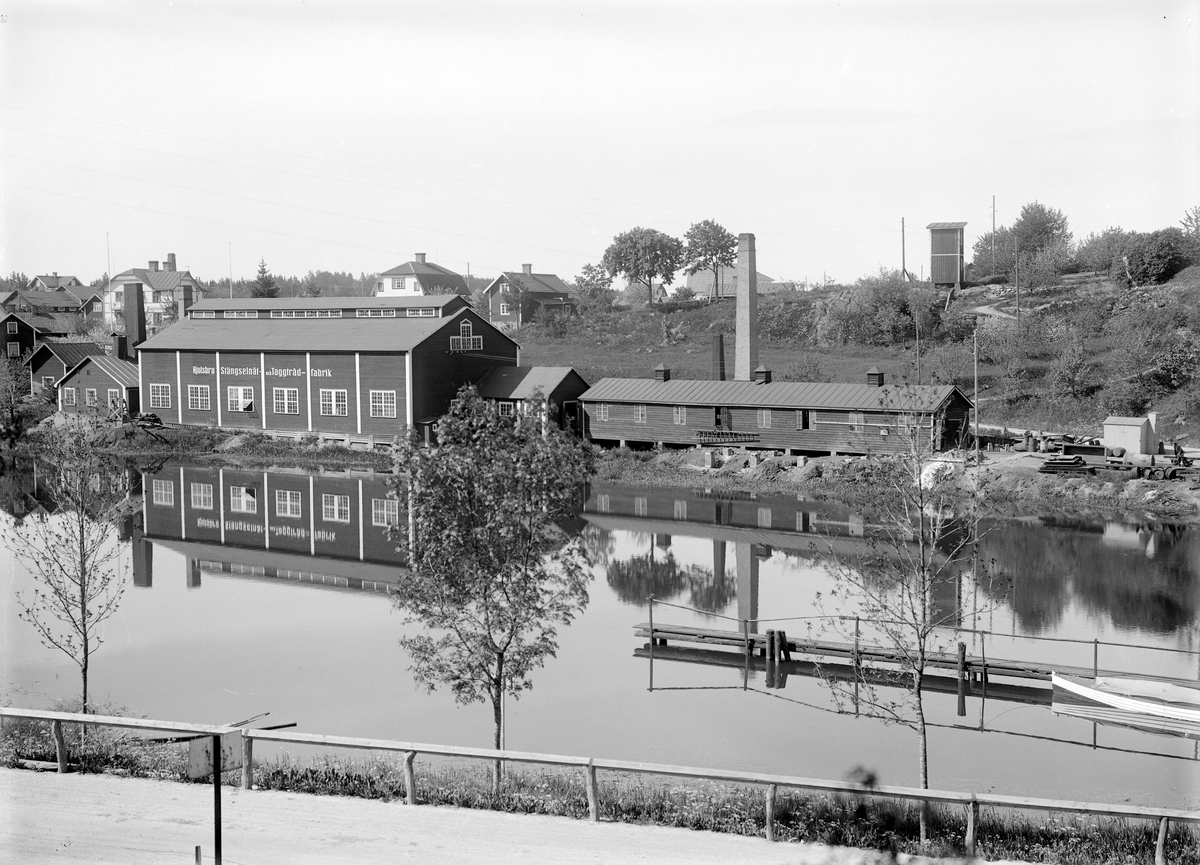 Den 25 juli 1907 registrerades Hjulsbro Tråddrageri- och Spikfabriks AB. Platsen var väl vald vid det gamla kvarnfallet med god tillgång på vattenkraft. Detta till trots kom företaget vid sämre marknadsläge på obestånd, men kunde rekonstrueras under ny ledning av entreprenören Jonn O. Nilson. Kort efter övertagandet 1923 kompletterades anläggningen med ny fabriksbyggnad för tillverkning av stängselnät och taggtråd. Här en vy mot den nya anläggningen något av 1920-talets senare år.