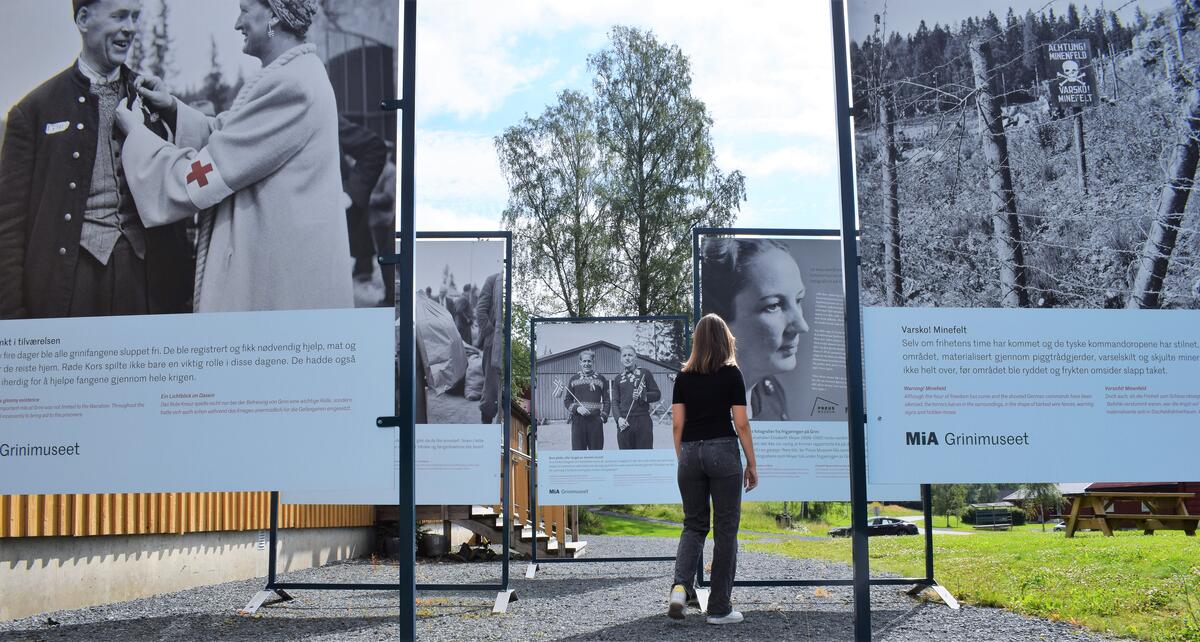 Fotografi tatt utenfor museet, ved uteutsillingen. En kvinne står midt i bilde med ryggen til og ser på plakatene om Grinis historie.