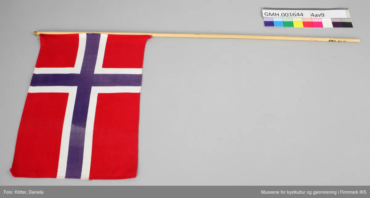 Ni norske flagg av eldre dato. Flaggene er av vevd bomullsstoff og omtrent like store. Pinnene er ulik lange, noen er knekt eller saget av, men alle har en kule, opprinnelig med gull maling på toppen.