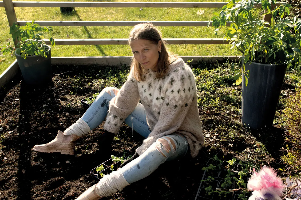 En kvinne sitter i et blomsterbed og graver i jorda