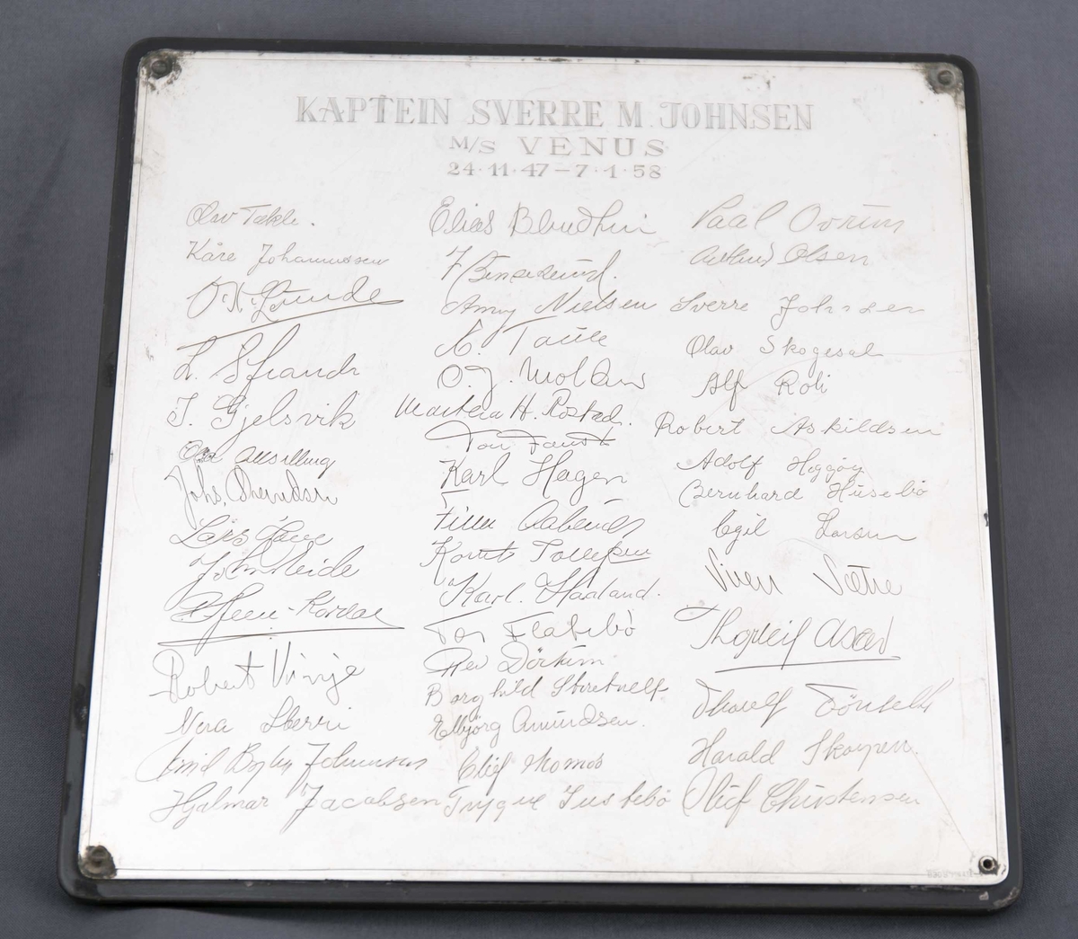 Plakett gitt til kaptein Sverre M. Johnsen på MS VENUS med signatur til mannskapet på skipet, datert 24.11.1947 - 7.1.1958. 
Kvaderatisk treplate påmontert inngravert sølvplate.