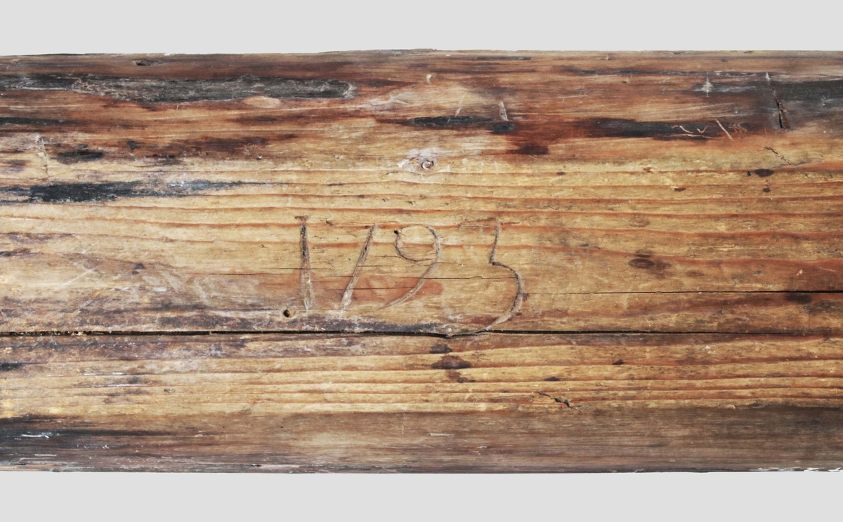 Baktråg. Rektangulärt, urholkat ur avlångt trästycke. Kortsidorna utskjutande som handtag. På undersidan skuret: "1793".