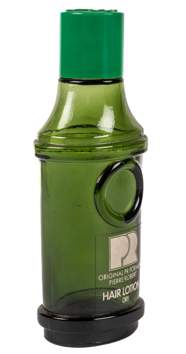 Flaska av brun-grönt glas med skruvlock i grön plast. Flaskan är ovalt rundad med bredare fram och baksida längst ned. Vid ca 2/3 höjd av flaskan finns en utstående list i glaset runt hela flaskan. Över den övre listen avsmalnar flaskan uppåt. Flaskan avsmalnar något nedåt mellan listerna. På framsidan under övre listen går en utbuktning i glaset. Under den står i vitt texten "PR ORIGINAL PR FOR MEN PIERRE ROBERT HAIR LOTION DRY". På locket i utstående bokstäver står det "PR". Fabrikationstryck i glaset i botten: "KG".