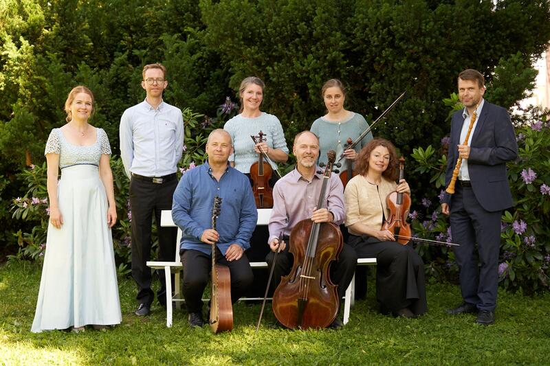 Åtte musikere fra ensemblet Nivalis barokk, fotografert ute i sommerlige omgivelser.