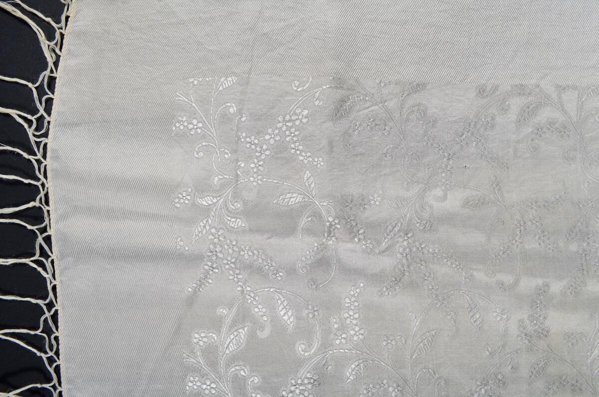 Hvitt, damaskvevd silkeskjerf med blomster- og bladmønster. Frynser på fire sider.