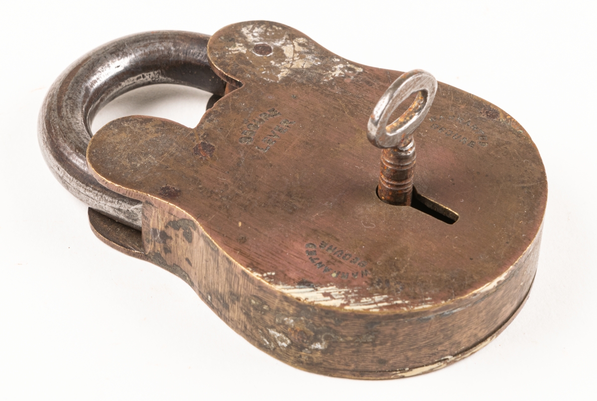 Lås, järn och mässing. Rundat nedtill. Nyckelhål på sidan med fastsittande nyckel. Märkt "Secure lever", "Warranted secured". Största bredd 6,4 cm.