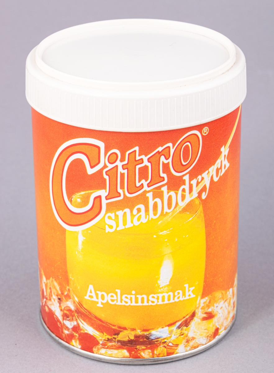 Cylinderformad plåtburk med plastlock, innehållet kvar. Orange pappersetikett, "Citro snabbdryck Apelsinsmak".