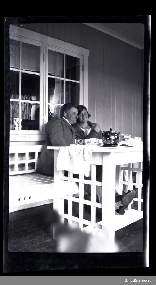 Två personer i en soffa vid ett uppdukat bord på en veranda.