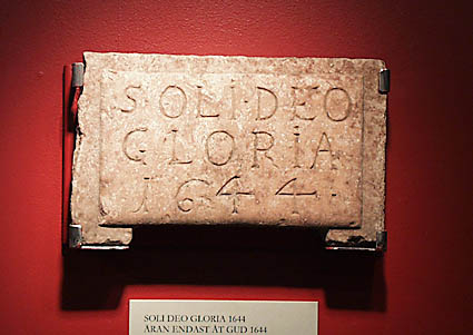 Byggnadsdetalj i röd kalksten. Upphöjt mittparti. Inskription: SOLI DEO GLORIA 1644 (Äran endast åt Gud 1644).