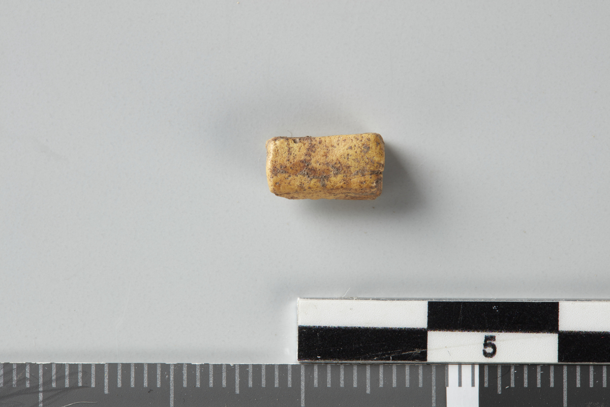 Katalogtekst 1995: 6: Fragment av gul perle med firkantet tverrsnitt. Stl. 0,9 cm. 