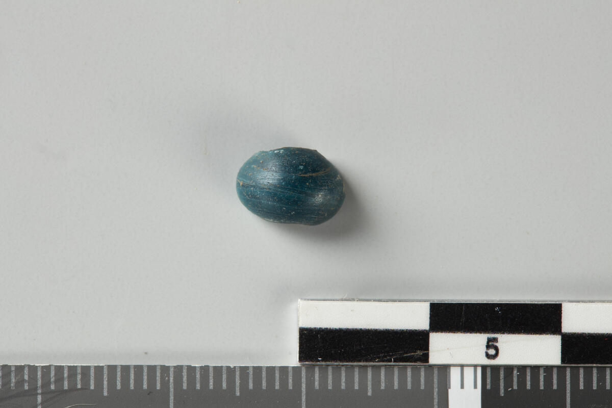 Katalogtekst 1995: 9: Fragment av blå, rund perle. Stl. 0,8 cm.