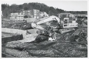 Grävmaskin och baracker i Kållereds centrum vid byggandet av trappa och järnvägsundergång cirka 1990. I bakgrunden till vänster ses lägenheterna på Streteredsvägen 1A - 1G, "Hemmet" och Brattåsgården.