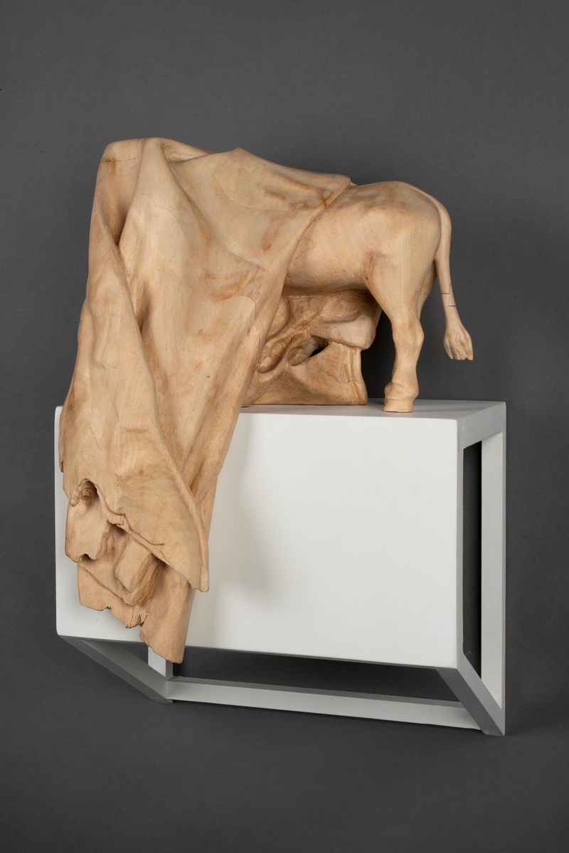 Treskulptur av en ku foldet inn i et tøystykke.