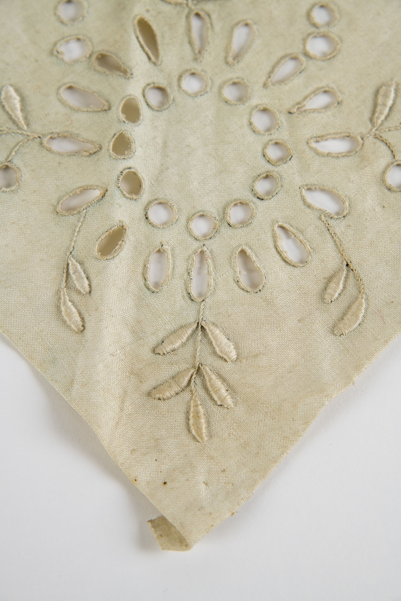 Trekantet stykke lin med et brodert midtmotiv og to "roser" på siden. Montert mot lyseblått silkepapir og med en etikett:  Ingertha Sviggum.