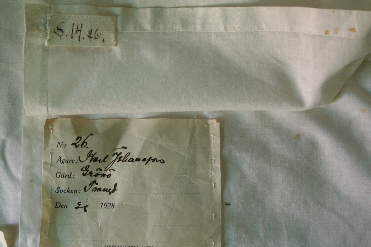 Kvadratiskt hals-eller huvudkläde av fin linne- eller bomullslärft. På två motstående sidor 7,2 cm bred fåll sydd med enkel hålsöm, på två sidor smal fåll.
Anteckning på påsydd lapp: Gammalt kläde från 1841.

Påsydd märkning S.14.26 troligen förväxlad märklapp.

Ingår i Textilinventeringen i Kronobergs län 1928-1930,
S.14.12, ägare Karl Johansson, Grönö.

/Birgitta Blixt 2022