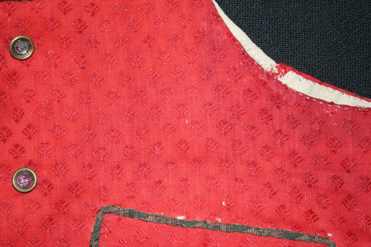 Kort väst i rött manufakturvävt kamgarnsylle med invävt mönster s.k. amens (rombmönster med dubbel kvist). Två framstycken/sidostycken, hög krage, dubbbelknäppt med 4 par metallknappar, upptill litet utvikt slag, knapphål på båda sidor. 2 st stolpfickor kantade med flerfärgat smalt band av siden eller slitet sammmetsband. Bandkantning längs framkanter, slag och krage till ca 7 cm in på kragens överkant. Knappar med rödfolierad mitt. 
Ryggstycket av fint linne, Foder i framstycken av samma linne.

Högtidsplagg. Se även DR 0063-0065. 

Elisabet Johansson/2019