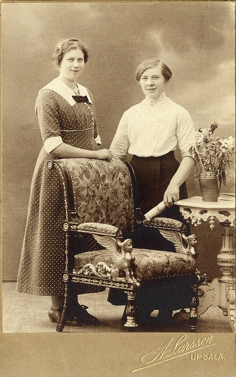 Två yngre kvinnor poserar för fotografen.
Under fotot text med blyerts: "Greta i Nöbbele".
Helfigur. Ateljéfoto.