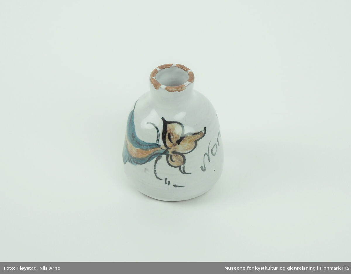 En liten keramikkvase med hvit glasur og dekor. 

Vasen er laget av keramikk, som består av typen porøst gods. Den er farget og har en lav brenningstemperatur. Vasen har en hvit glasur på både innsiden og utsiden, som dekker hele vasen bortsett fra bunnen. Bunnen har den naturlige rødbrune fragen til porsøt gods, med en grov og porøs overflate. Vasen har en smal og kort hals med en bred sirkulær korpus (kropp), som utvider seg gradvis fra halsen og  ned til bunnen der den snevres inn. 

Vasen er dekorert med påmalt blomstermotiv som går rundt nesten hele vasen, og "Nordkapp" malt i sort.Kanten på munningen er malt i brunt.