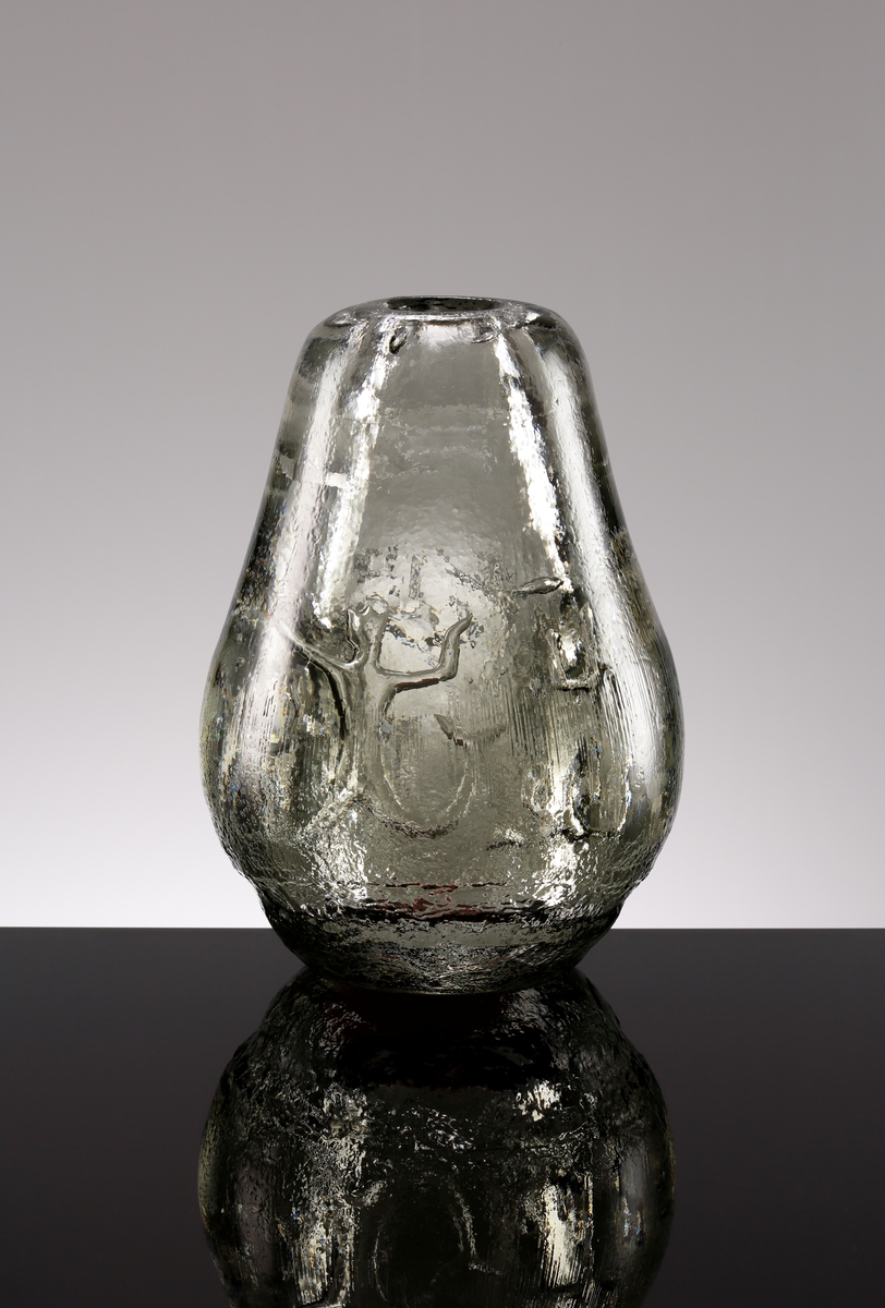 Formgiven av Edvin Öhrström. Arielvas, päronformad i ljusgrått glas. Dekor bestående av abstrakt luftmönster förställande Neptunus, sjöjungfrur och fiskar. Vasens utsida reliefmönstrad.
