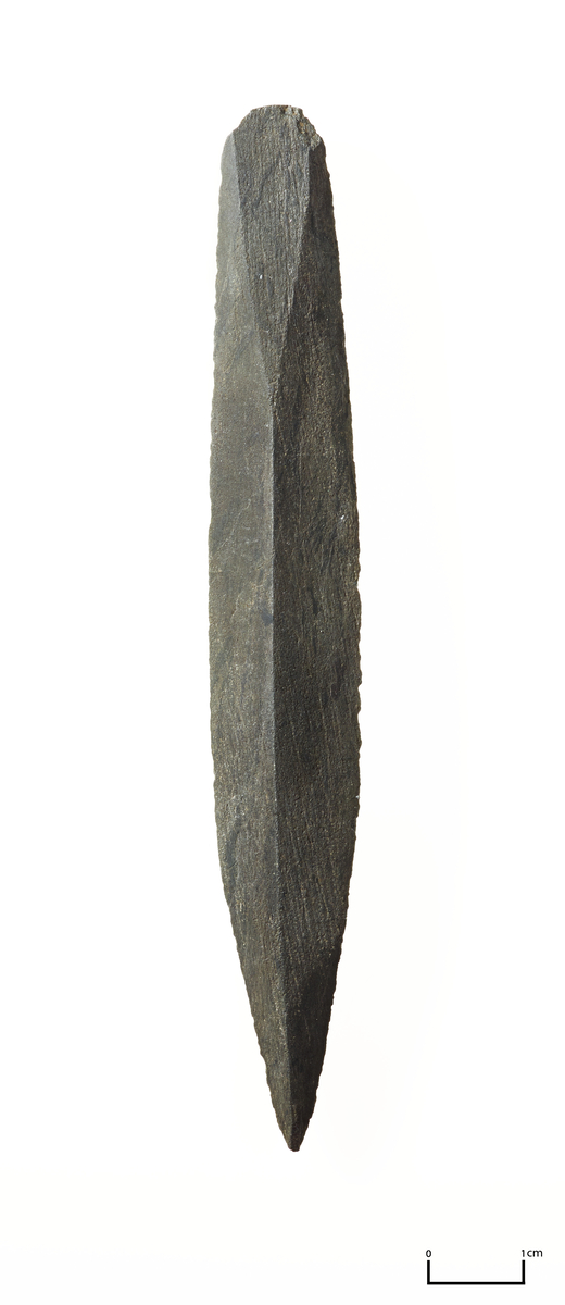 Elegant, rygget skiferpil med lett konvekse egger, rombisk tversnitt og trekantede festefasetter (type G. Gj. 132). Av grå skifer. Mrk. "B. 14, 75 cm d.". Litt. Utne 1973, fig 37 a.