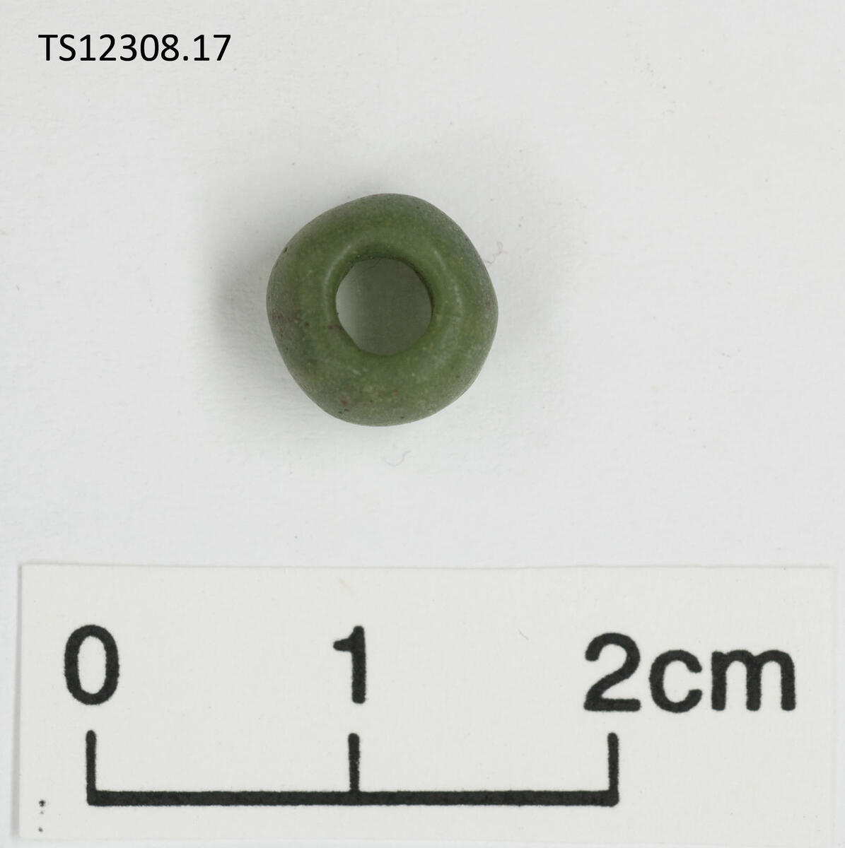 1 stk perle av glass. Grønn. Rundede sider, ujevn form. 0,9 cm i diameter, 0,7 cm tykk.