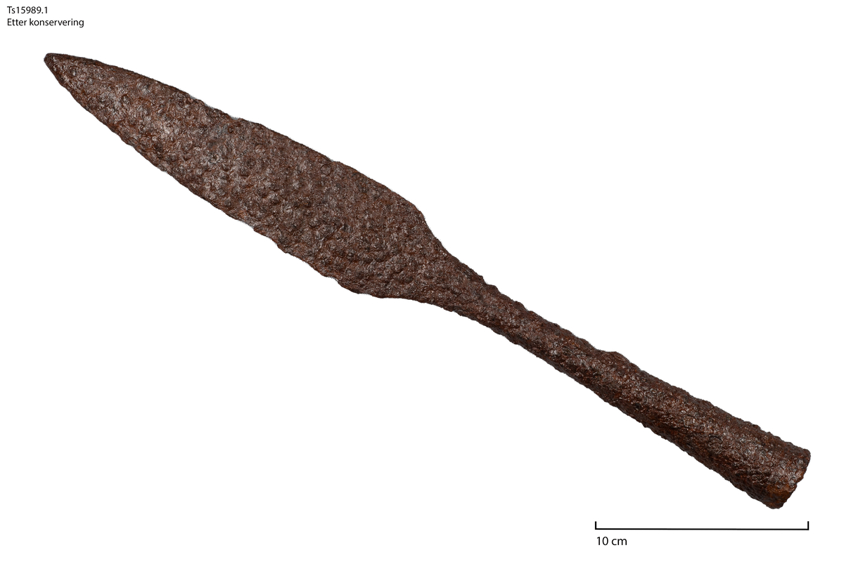 Spydspiss av jern. Likhetstrekk med Solbergs type XI som dateres til perioden 950-1050 evt. Det ble også funnet rester etter (forkullet?) tre inne i skaftet. Nederst på falen er det et lite festehull samt en linjedekor som følger falens diameter.