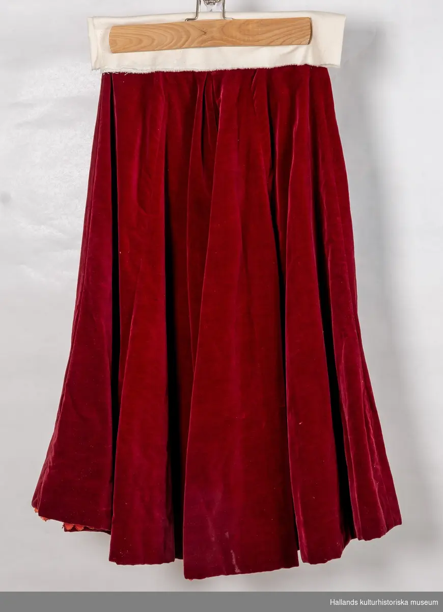 Maskeraddräkt av vinröd sammet bestående av lång kjol, knäbyxor och jacka.