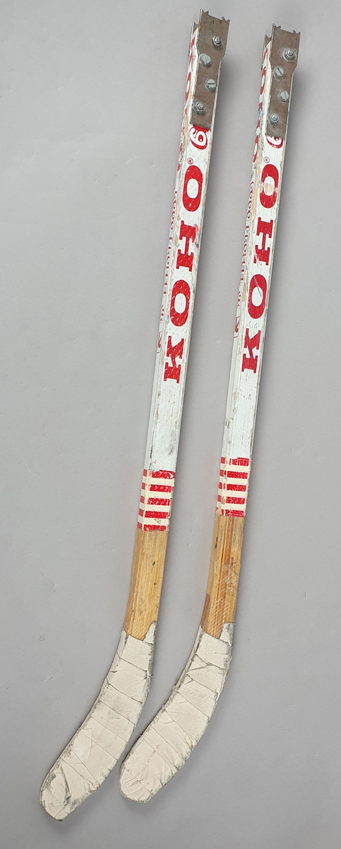 To ishockey-køller av tre, med metallbeslag på den ene kortsiden, for feste på kjelken.