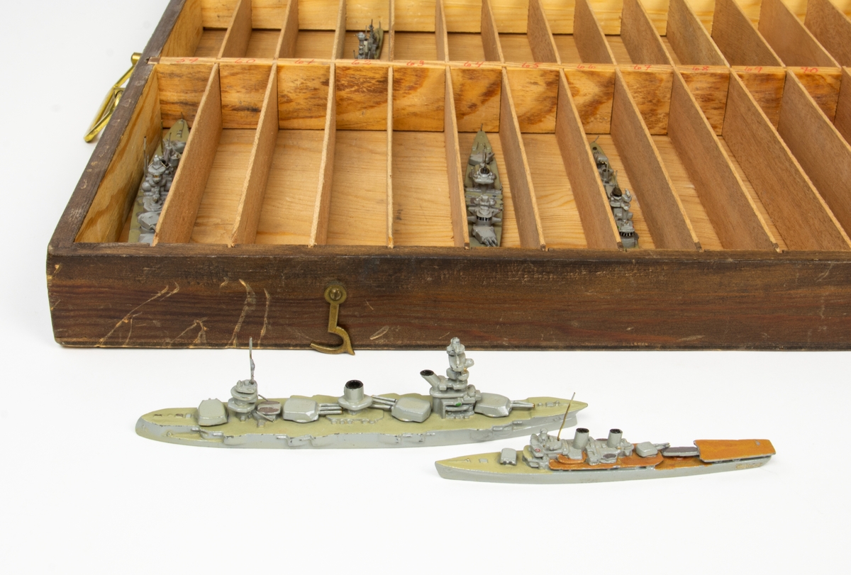 Modellfartyg i trälåda med 87 numrerade fack för olika fartyg. I locket en förteckning av fartygens placering i lådan. Fartygen är gjutna i metall. De flesta av fartygen saknas i lådan.