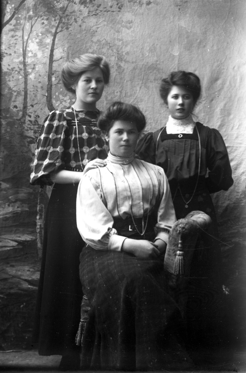 Atelierfoto.Tre yngre kvinner.En sitter og de to andre står.