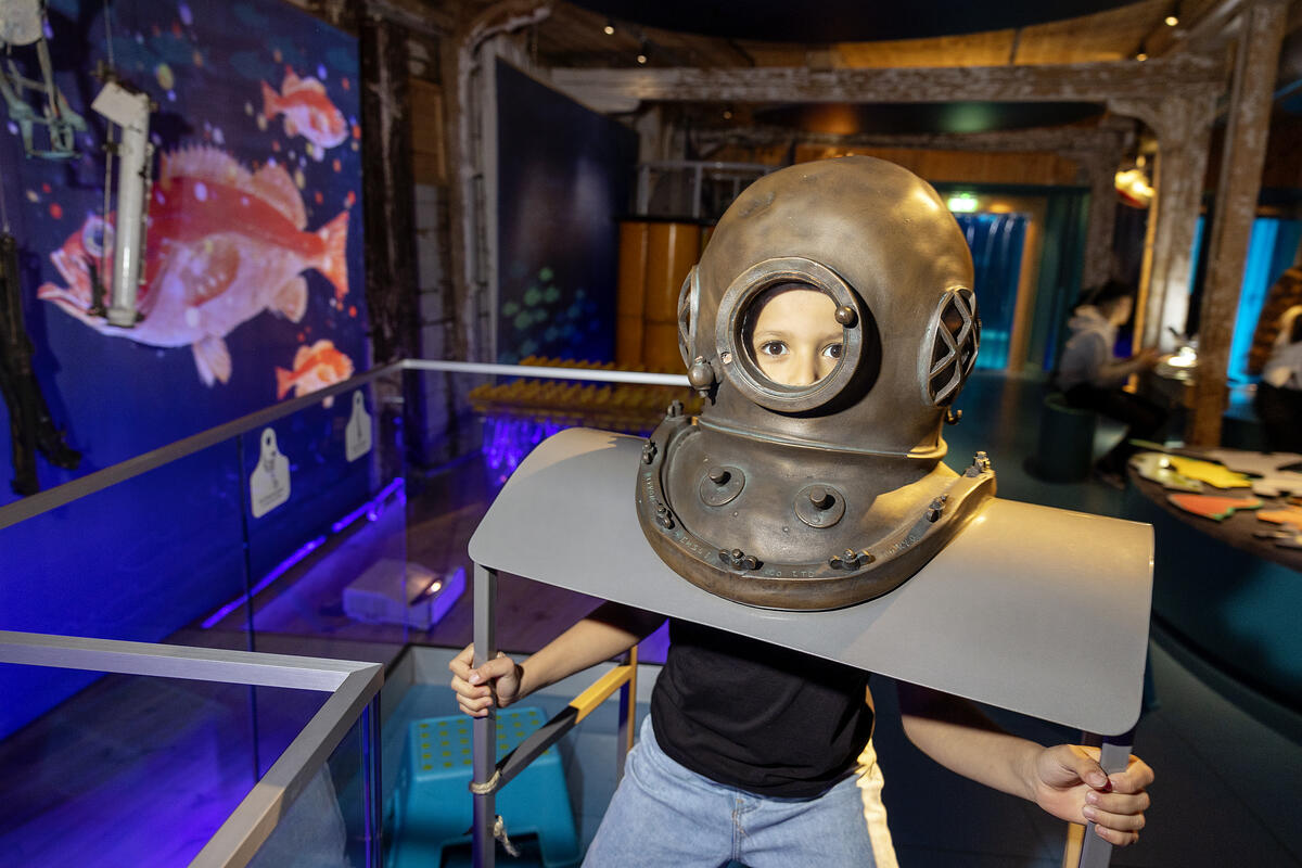 En liten gutt har stukket hodet opp i en gammel dykkerhjelm i utstillingen verden under vann