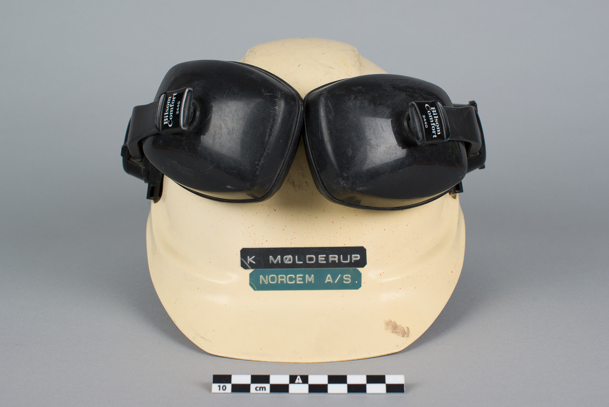 Hjelm påmontert hørselvern. Pålimt bilde av Pluto bak. Hjelmen ble brukt av Knut Mølderup som jobbet med vedlikehold, ABT.