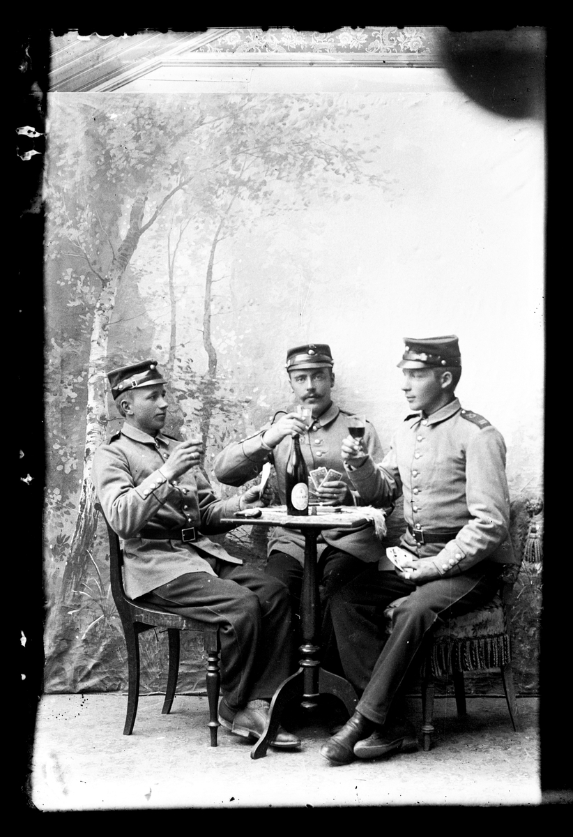 Atelierfoto. Helfigurer. Tre soldater sitter ved et bordm spiller kort og drikker.