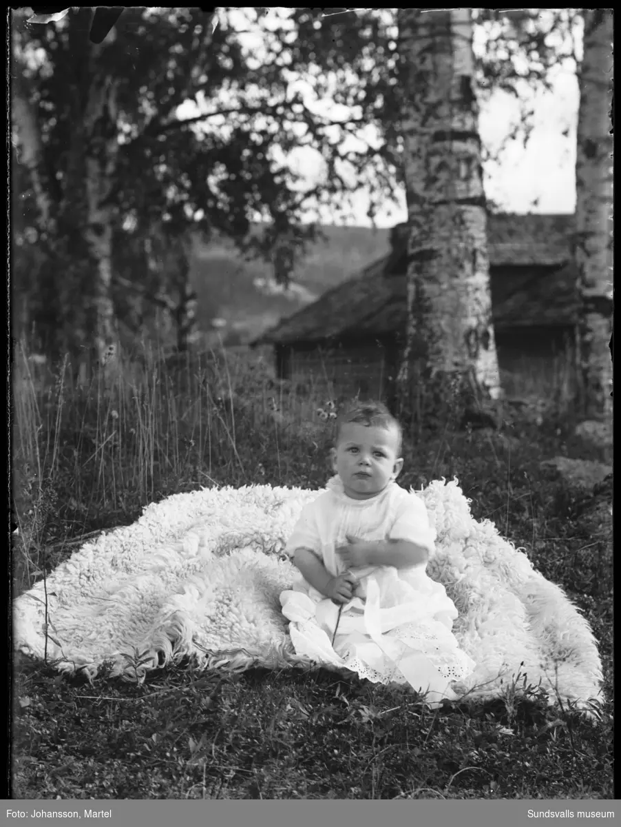 Porträtt av en baby som sitter i gräset på en fäll.