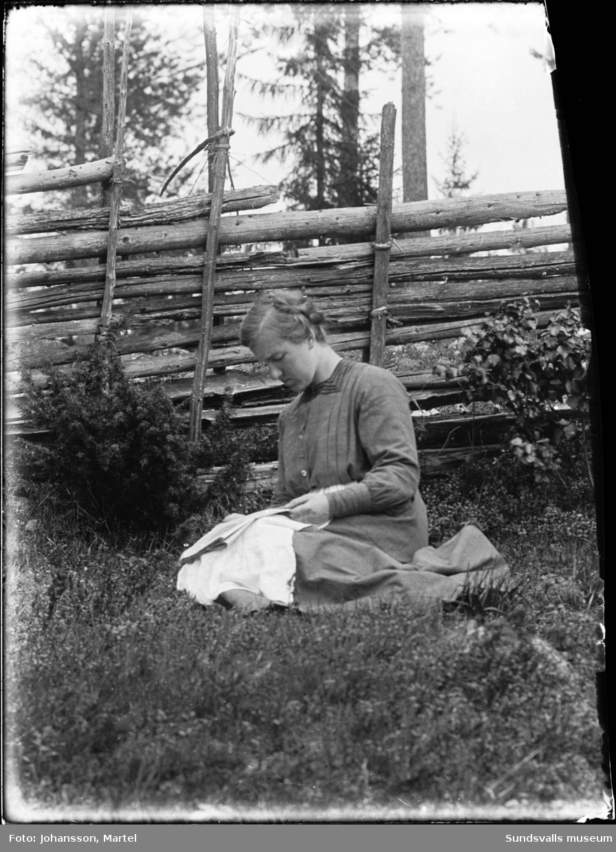 Märta Johansson på Brännsvedjan sitter invid en gärdesgård och läser tidningen.