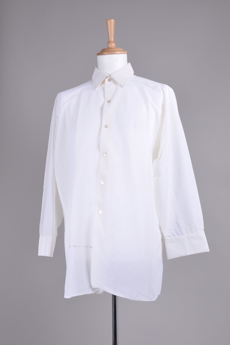 Skjorte til mann. Hvit, nylon. Lange ermer, krage, seks knapper foran og knapp på hver mansjett.