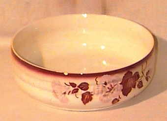Cirkelformat keramikstycke med rosa blommor och bruna blad, samt med bruntonad överkant.