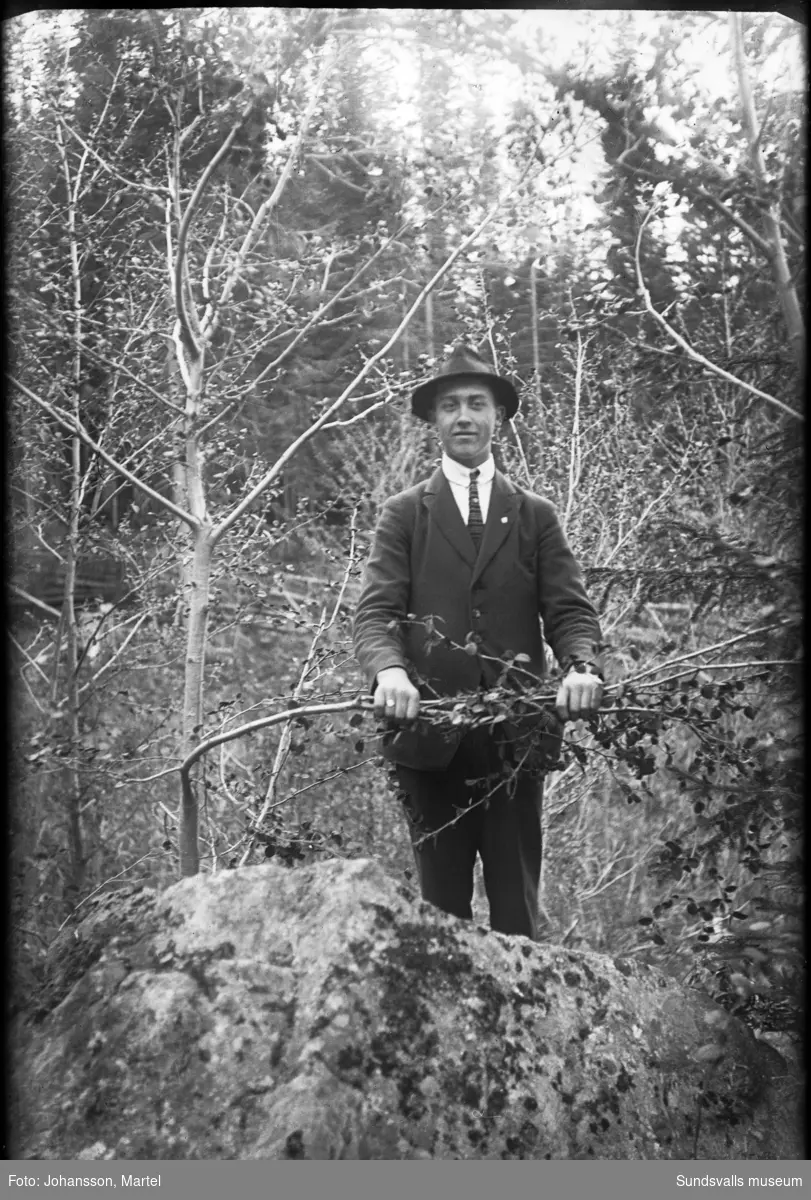 Porträtt i skogsmiljö av en ung man i hatt.