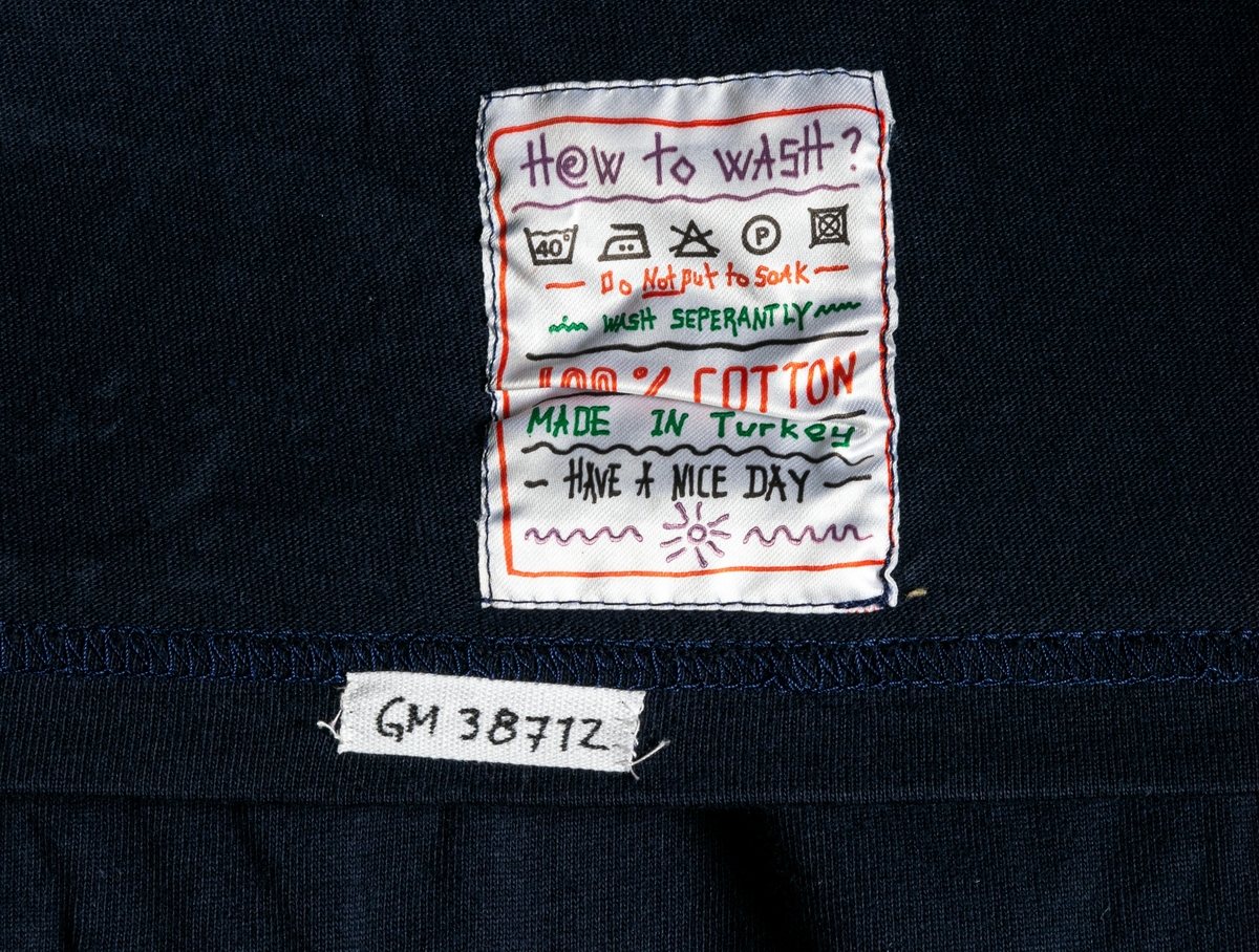 T-shirt i marinblå och magenta med flerfärgad broderad text och etikett.