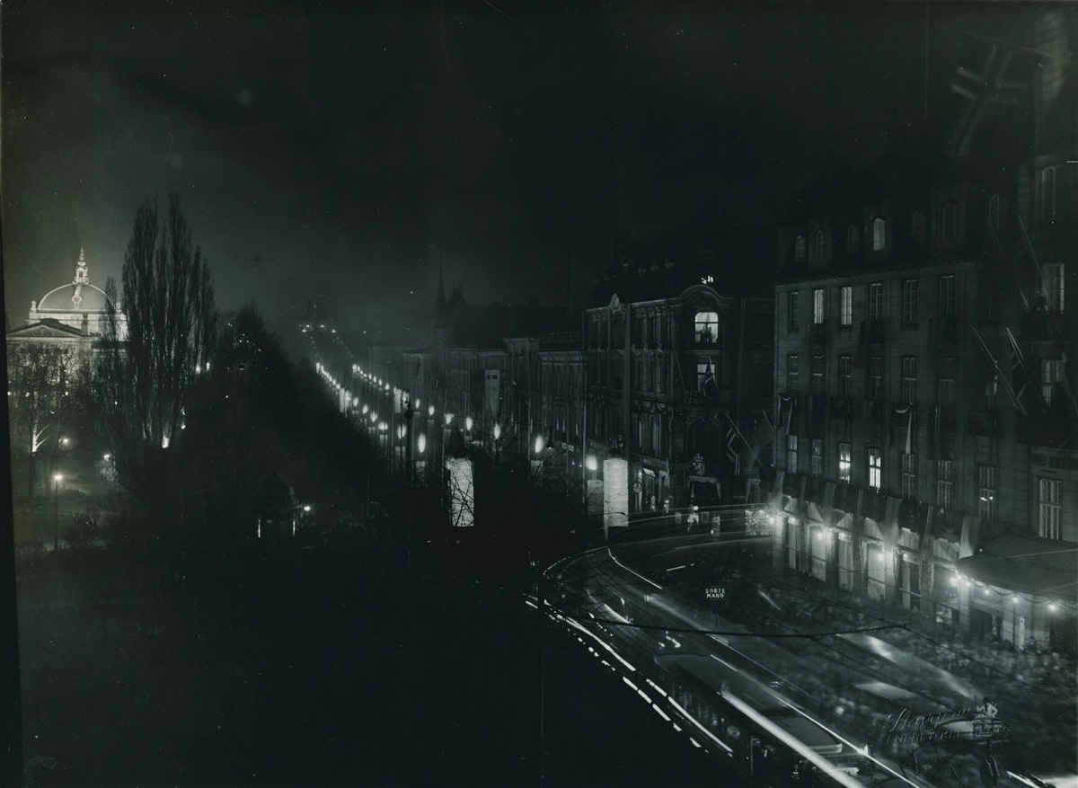Kveldsbilde av Karl Johans gate. Elektriske gatelys. Nationaltheateret ses i bagrunnen.