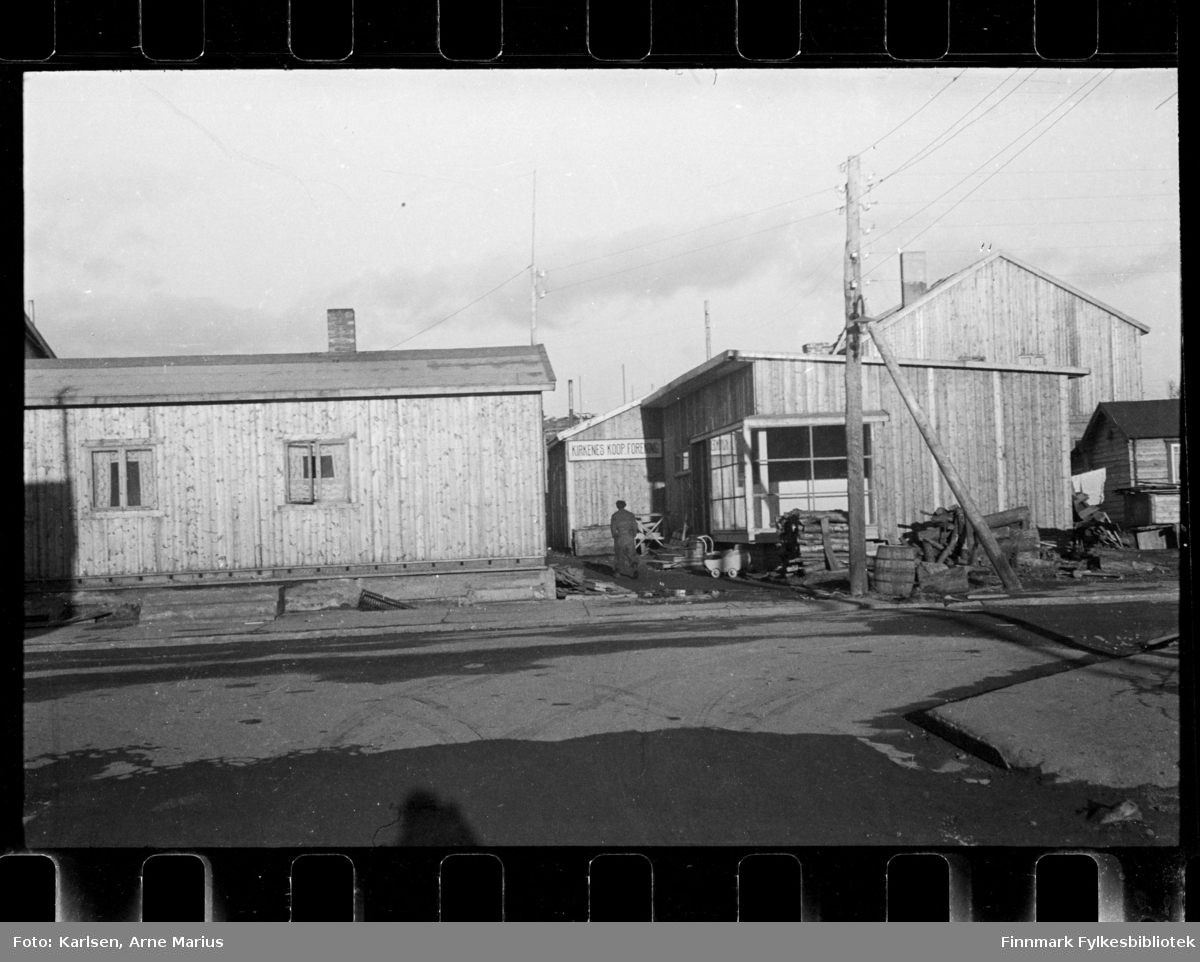 Foto av bygget til Kirkenes Kooperative forening, foto antagelig tatt i perioden 1945 - 1949

Utenfor bygget kan man se en barnevogn og en mann 