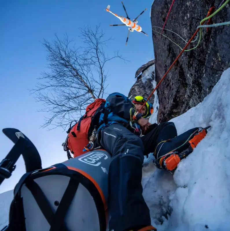 Mann med klatreutstyr opp ein bratt fjellskrent i snø