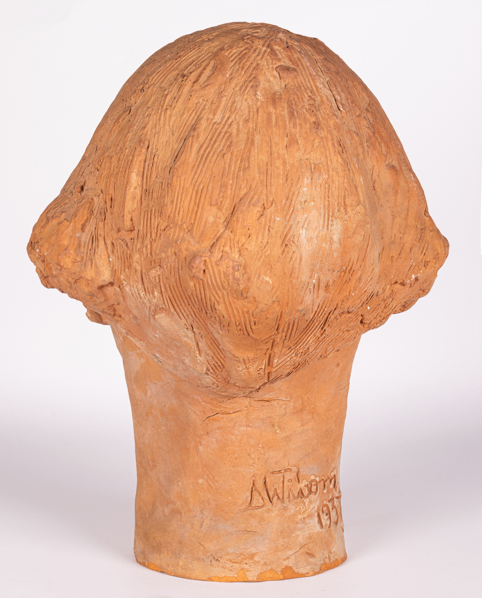 Porträttbyst i bränd lera av skulptör och keramiker Maggie Wibom, 1937. Bysten är med mycket stor sannolikhet ett självporträtt av konstnären, då den har flera karakteristika med Maggie Wibom, som frisyr, ögonbryn, ögon och näsa. Maggie Wibom har även i unga år, under tiden vid Tekniska skolan, utfört självporträtt i lera, vilket finns dolumenterat på foton.