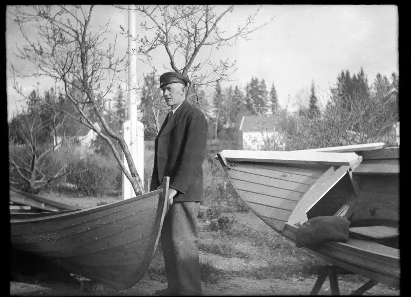 En mann står mellom to trebåter som han har bygget.