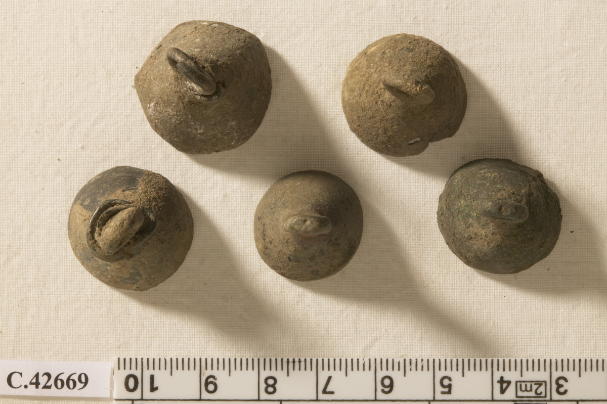5 small bells, probably part of a piece of jewellery. Two incised lines on the outside around the rim. The clappers are missing and were probably made of iron. Two of the bells have a hole near the loop, which allows a wire to enter the bell.