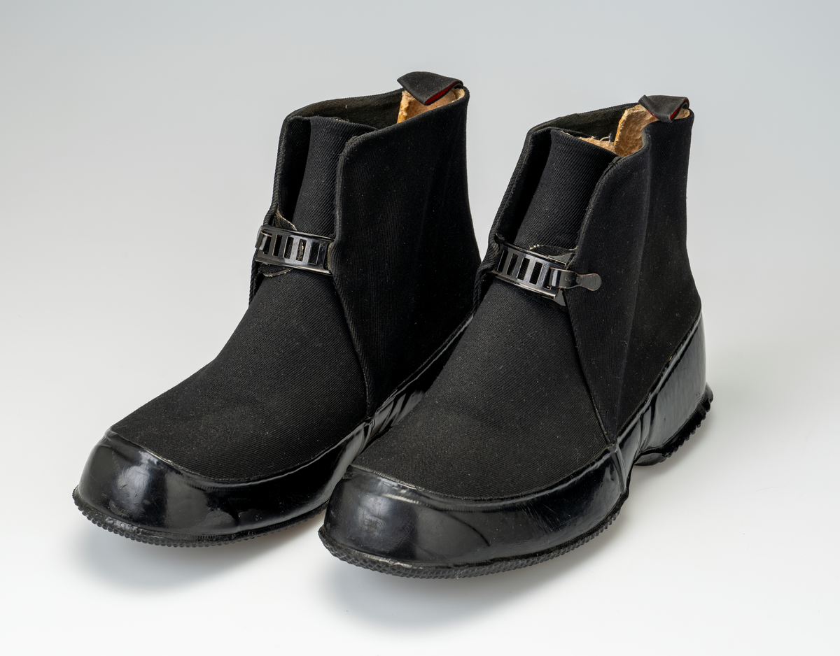 Et par overtrekkssko til herre fra Viking-Askim. Skoene har en svart gummisåle som går opp i en stor kant rundt forbladet. Overdelen av skoen er sydd av slitesterkt svart bomullsstoff. Det er åpning foran på skoen. En metallspenne åpner/lukker skoen. Under spennen er det en tunge av svart tekstil. Den er sydd slik at det er tett på hver side av tungen. Skoene er foret med tekstil og ullstoff. Oppe bak på skoene er det en hempe med merkenavnet.