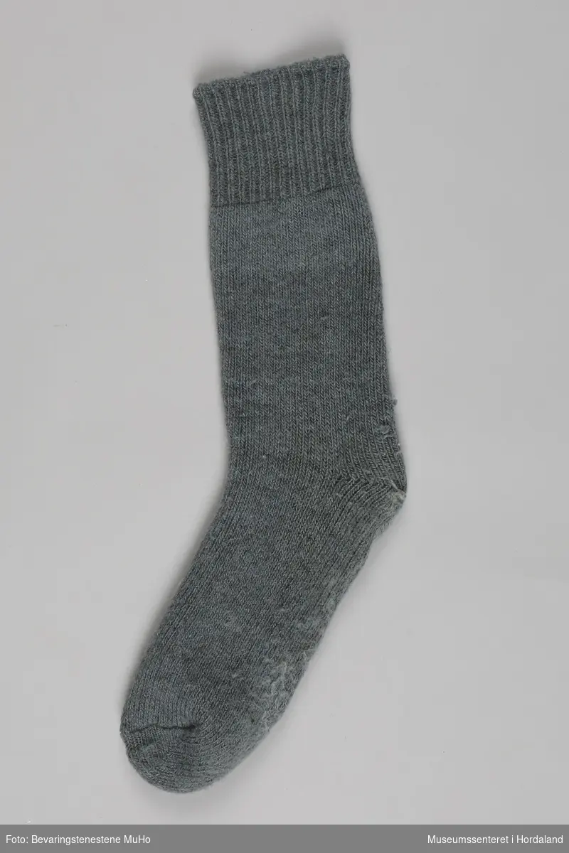 Eit par grå strikka sokkar med halvlangt brot, godt brukte. Den eine sokken er stoppa på hælen med lyseblått garn.