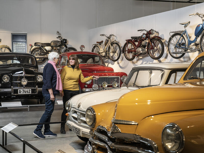 Bildet viser to besøkende på Norsk kjøretøyhistorisk museum, med mange eldre kjøretøy rundt seg.
